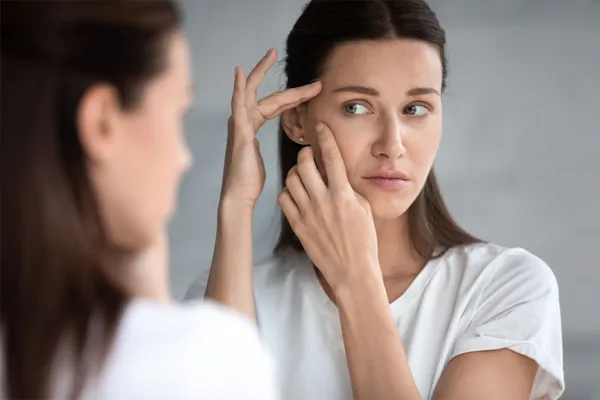 A woman checks her face for acne in the mirror. Schedule treatment for acne and acne scars from Yashoda Singh, MD in Hamilton-Toronto-Niagara.