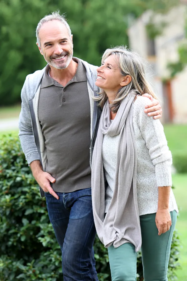 A mature couple in gray toned clothes and jeans walk happily outside, happy with their successful bioidentical hormone treatments from Yashoda Singh, MD in Hamilton-Toronto-Niagara.