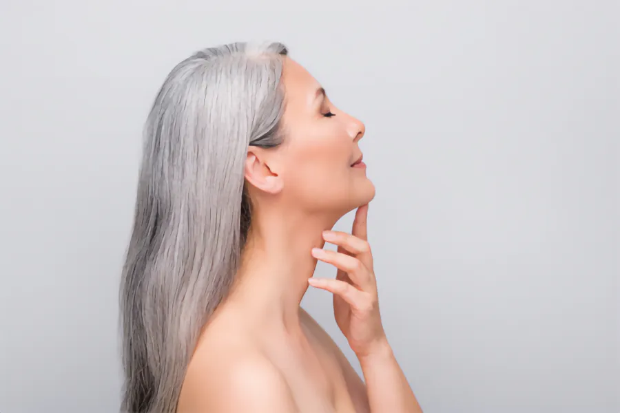 A mature Asian woman seen in profile touching her well-shaped chin. Schedule belkyra chin fat reduction treatment from Yashoda Singh, MD in Hamilton-Toronto-Niagara.