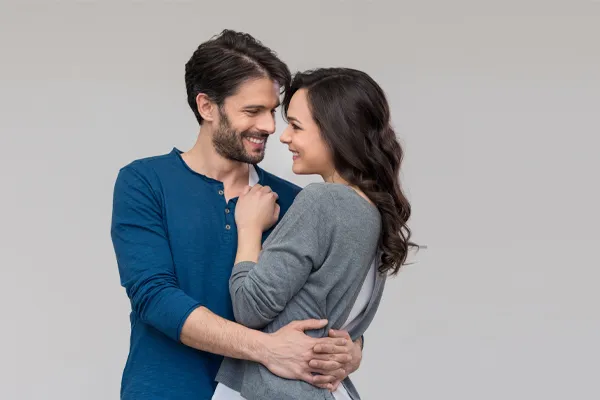 A man in a blue shirt embracing a woman in a gray shirt smiles due to his successful erectile dysfunction care from Yashoda Singh, MD in Hamilton-Toronto-Niagara.