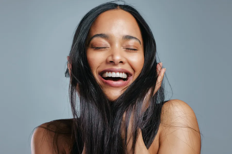 A woman runs her fingers through her long, thick, lustrous hair. Get exosomes for hair restoration from Yashoda Singh, MD in Hamilton-Toronto-Niagara.