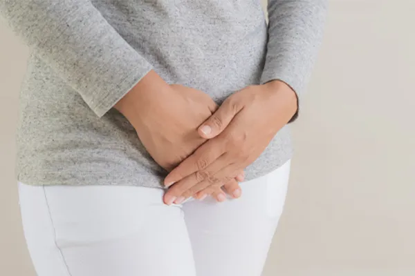 Close up of a woman in a gray shirt and white pants holding her hands below her abdomen in discomfort. Get treatment for fibroids from Yashoda Singh, MD in Hamilton-Toronto-Niagara.