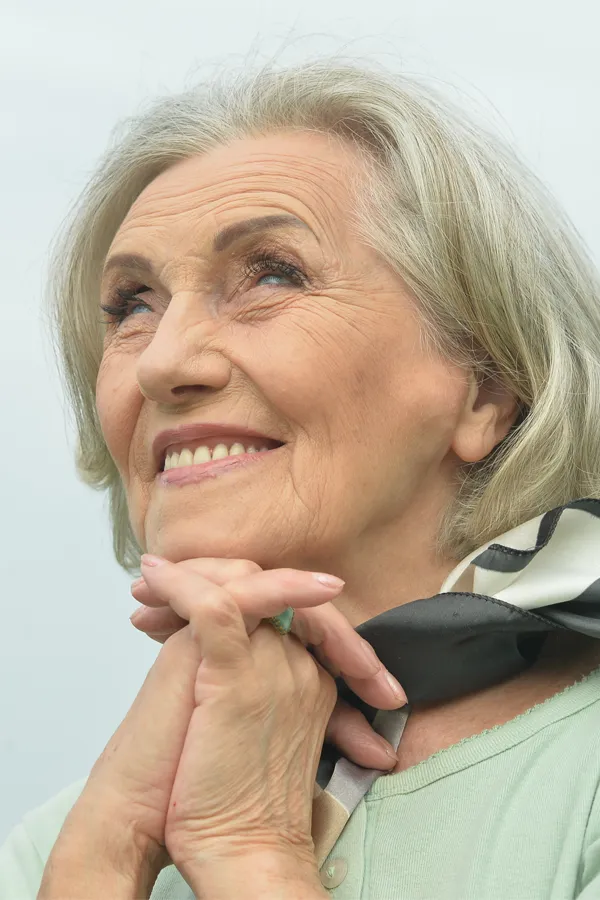 An older woman holds her hands together under her chin and looks up at a cool sky smiling. Get treatment for hot flashes and night sweats from Yashoda Singh, MD in Hamilton-Toronto-Niagara.