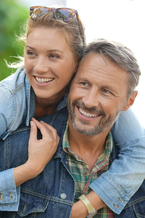 A couple in denim jackets embrace playfully outdoors. Get hypogonadism treatment from Yashoda Singh, MD in Hamilton-Toronto-Niagara.