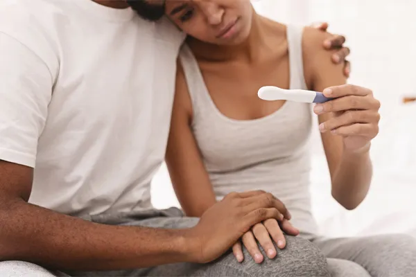 A couple look at a pregnancy test with disappointment. Get male infertility treatment from Yashoda Singh, MD in Hamilton-Toronto-Niagara.