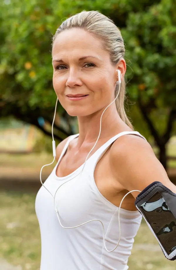 A fit middle aged woman wearing earphones and a tank top smiles after a run. Get insulin resistance treatment from Yashoda Singh, MD in Hamilton-Toronto-Niagara.