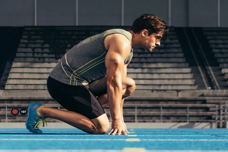 A white man kneels at the starting line on a track, determined to do his best. Get treatment for lean muscle loss and recovery from Yashoda Singh, MD in Hamilton-Toronto-Niagara.
