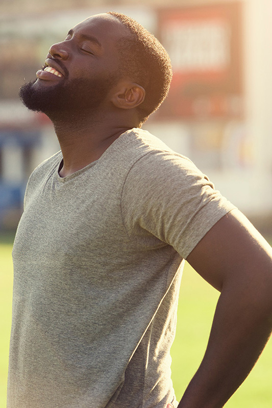 A black man in a gray t-shirt and smiles, looking up with closed eyes after a satisfying workout. Get treatment for lean muscle loss and recovery from Yashoda Singh, MD in Hamilton-Toronto-Niagara.