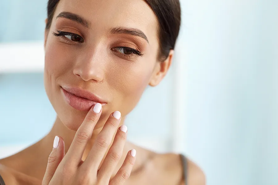 A beautiful woman smiles and touches her lips. Get lip enhancement treatment from Yashoda Singh, MD in Hamilton-Toronto-Niagara.