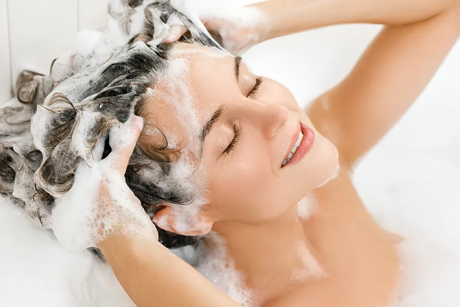 A woman shampooing her hair in the tub. Get medical grade hair care from Yashoda Singh, MD in Hamilton-Toronto-Niagara.