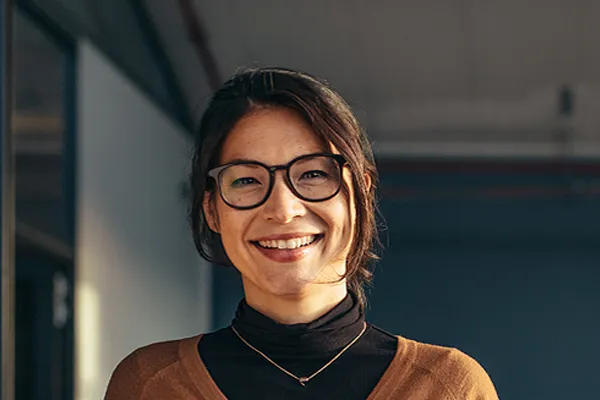 A brunette woman with glasses smiles in a gray-blue walled office. Get metabolic syndrome from Yashoda Singh, MD in Hamilton-Toronto-Niagara.