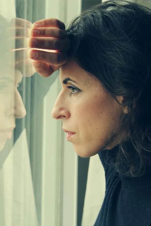 A brunette woman in a thin dark turtleneck looks out the window with a serious expression, suffering from PCOS. Get treatment for Polycistic Ovarian Syndrome/PCOS from Yashoda Singh, MD in Hamilton-Toronto-Niagara.
