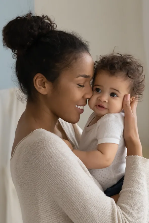 A black woman happily touches her forehead to her infant's head. Get treatment for postpartum hormone imbalance from Yashoda Singh, MD in Hamilton-Toronto-Niagara.
