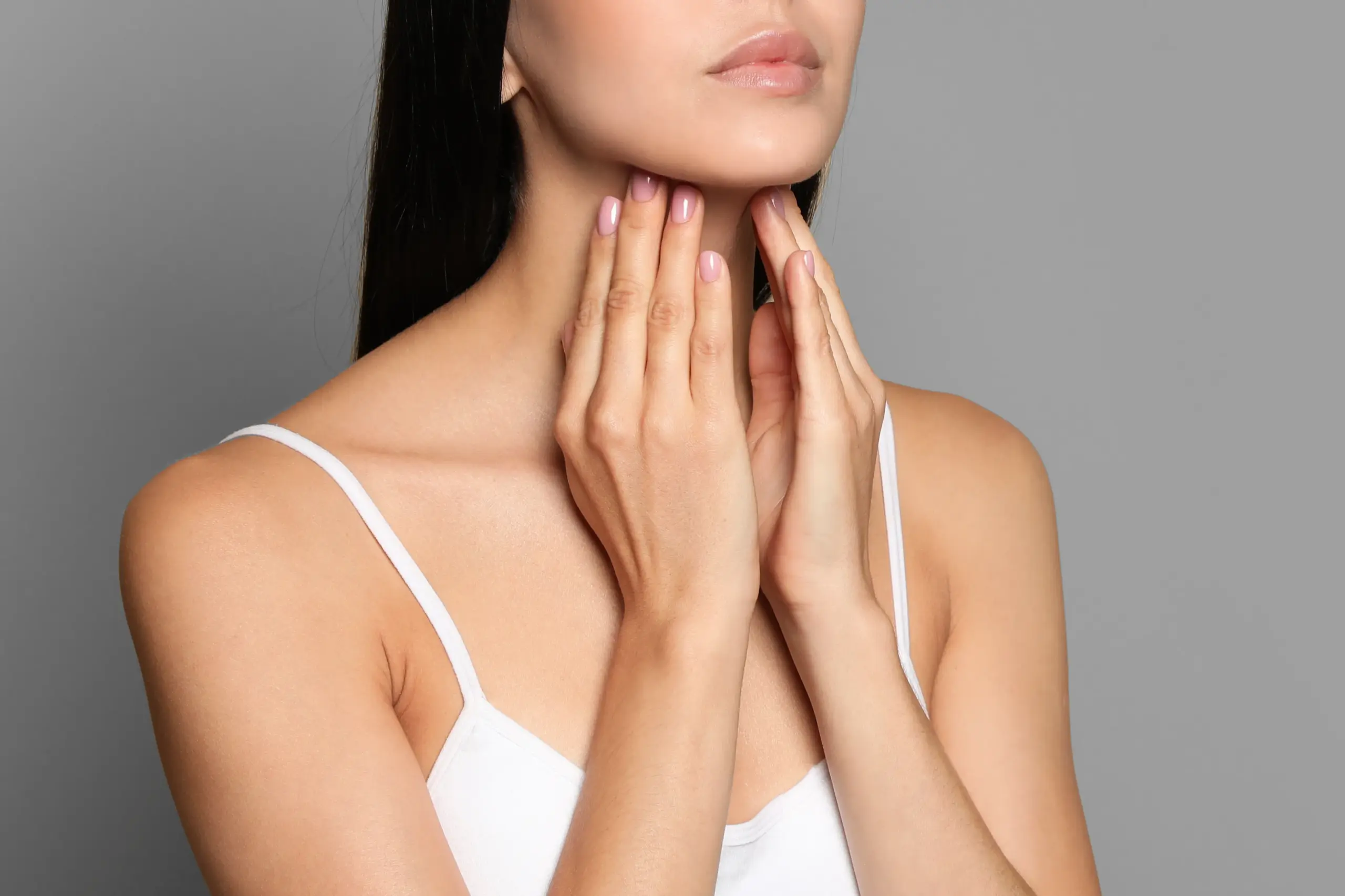 A woman in a white tank top touches her neck looking for signs of thyroid disorder. Get help for thyroid disorders from Yashoda Singh, MD in Hamilton-Toronto-Niagara.