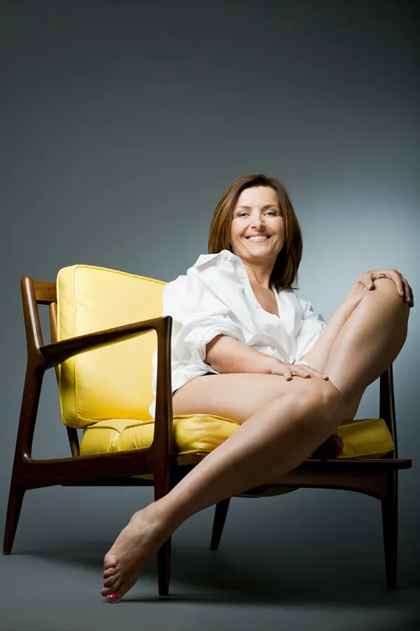 A middle-aged woman sits in a chair showing her smooth, featureless legs. Get vein and lesion removal treatment from Yashoda Singh, MD in Hamilton-Toronto-Niagara.
